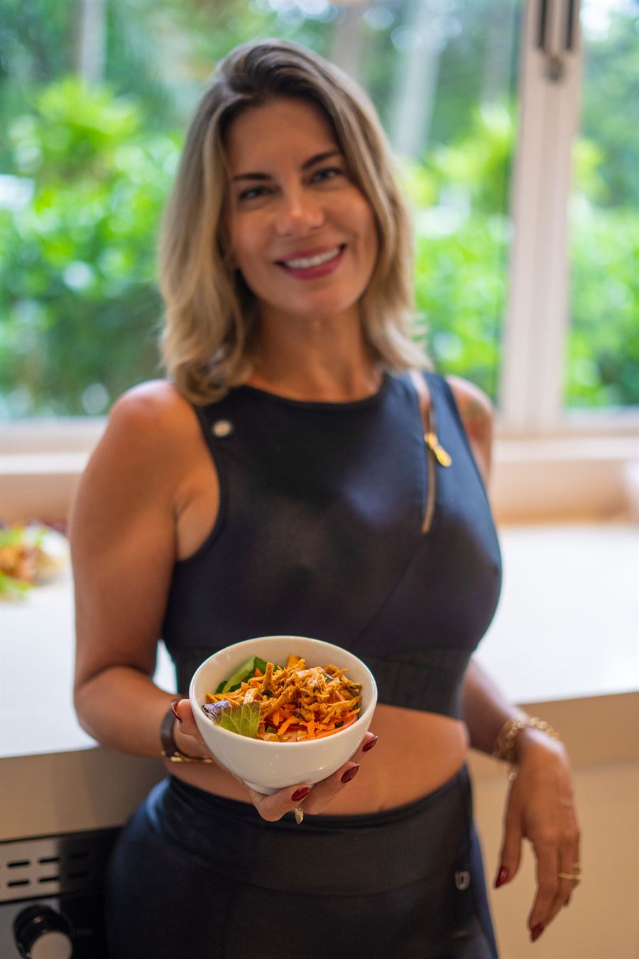 Nutri Luciana Alves sorrindo, de roupa de treino, segurando um bowl de comida