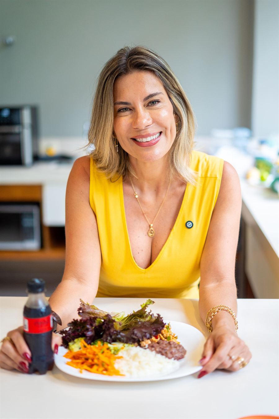 Nutri Luciana à mesa com um prato de arroz, feijão, carne, cenoura e salada